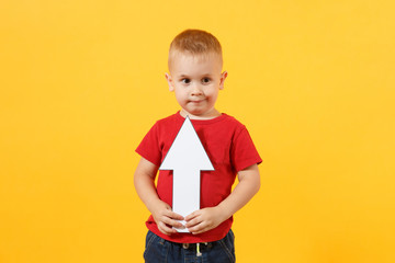 Little cute kid baby boy 3-4 years old in red t-shirt holding in hand up arrow isolated on yellow background. Kids childhood lifestyle concept. Appreciation of exchange rates. Copy space advertisement