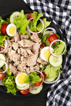 Salad with tuna, anchovies and vegetables. Mediterranean food. The background is black. Top view. Copy space.  Vertical shot.