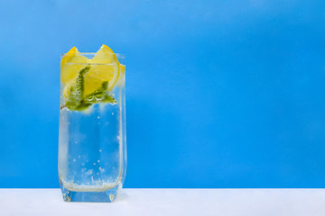 Mineral infused water with lemons and mint leaves on blue background.