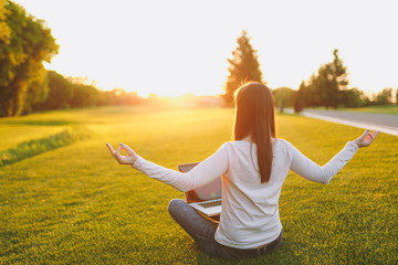 Young calm student female in casual clothes. Woman sitting, relaxing, hands in yoga gesture. Laptop pc computer on green grass ground sunshine lawn outdoors. Mobile Office. Freelance business concept.