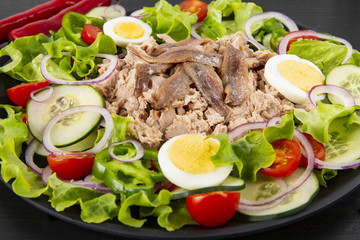 Salad with tuna, anchovies and vegetables. Mediterranean food. The background is black. Top view. Copy space. Horizontal shot.