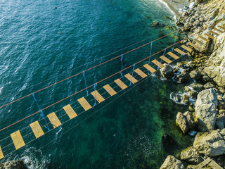 aerial view of rope bridge between the rocks over the sea and danger waves and stones