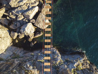 aerial view of rope bridge between the rocks over the sea and danger waves and stones
