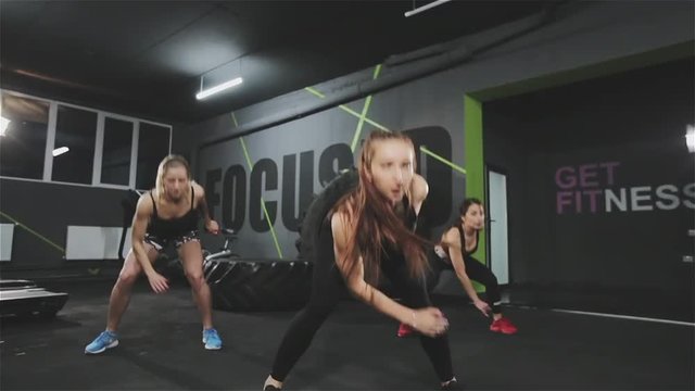 Young athletic woman jumping and exercising in team in modern dark gym.