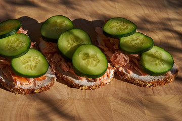 Close up Picture of three open sandwiches with creamy cheese, smoked salmon and slices of fresh cucumber served served on the wooden plate in garden bistro as light dish.    