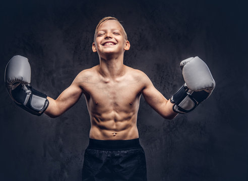 Young shirtless boy boxer with boxing gloves have fun while posing in a studio. Isolated on the dark textured background.