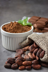 Cocoa beans, powder and chocolate on gray stone background.