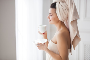 Beautiful woman in the towel after bathing drinking morning coffee