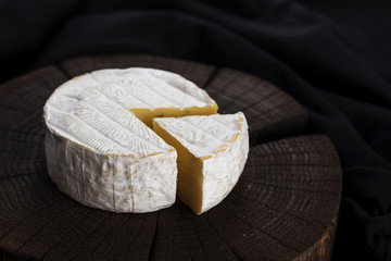 Camembert cheese on black wooden background, with copy space. Shallow depth of field