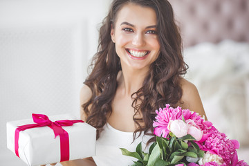 Very beautiful woman with flowers and gift indoors