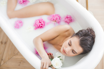 Obraz na płótnie Canvas Young beautiful woman taking bath with flowers and milk
