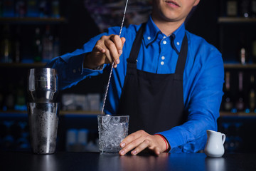 A smiling bartender stirring ingredients in a glass in order to prepare and serve a chilled...