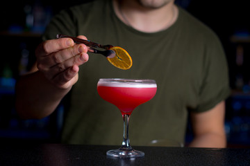 The bartender decorates Morro cocktail with dried orange slice