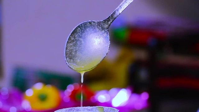 hand holds spoon with flowing ghee and dripping