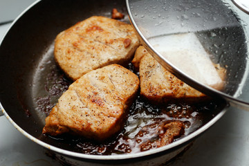 A close up of greasy pieces of pork in a frying pan. 
