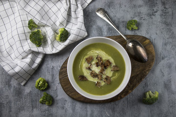 Top view of served brocoli creamy soup with cream and bread croutons on rustic table with spoon and fresh brocoli - photo with selective focus