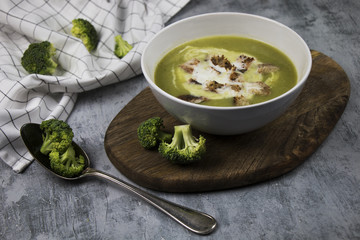 Photo of served brocoli creamy soup with cream and bread croutons on rustic table with spoon and fresh brocoli - photo with selective focus