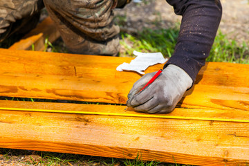 The builder left-handed measures the tape measure with a pencil and marks with a pencil