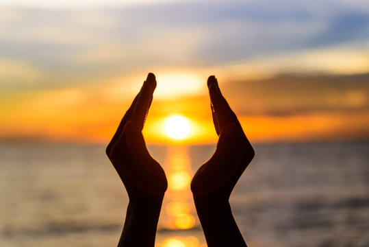 Woman hands holding the sun during sunrise or sunset.
