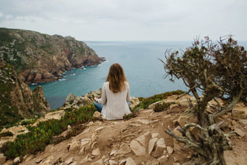Woman on a cliff sitting and meditating and watching the landscape