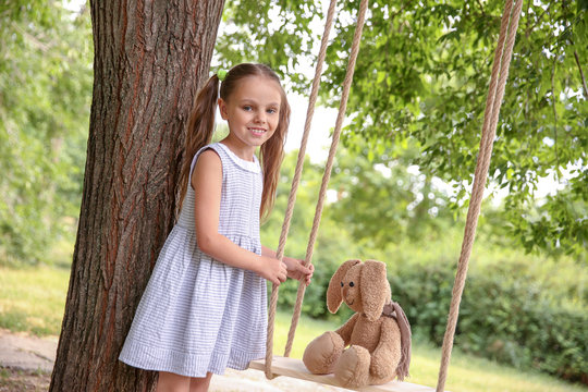 Cute little girl pushing bunny toy on swing outdoors