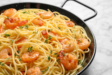Frying pan with spaghetti and shrimps on light background