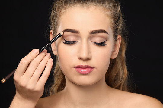 Young woman undergoing eyebrow correction procedure on dark background