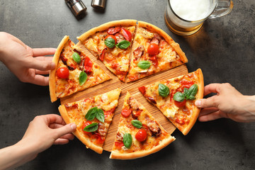 People taking slices of delicious pizza with tomatoes and sausages at table
