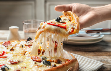 Woman holding slice of delicious hot pizza over table, closeup