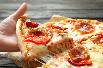 Woman holding slice of delicious hot pizza over table, closeup