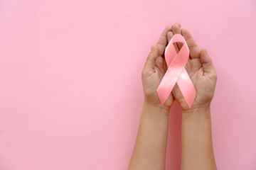 Woman holding symbolic ribbon of breast cancer awareness on color background, top view....