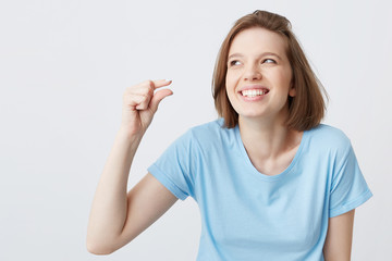 Cheerful beautiful young woman in blue t shirt laughing and showing tiny size by fingers of her hand isolated over white background