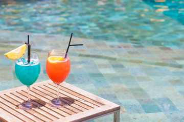 two perfect orange and blue exotic cocktails on the table, pool background