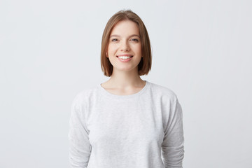 beautiful woman expresses happy emotions, has broad pleasant smile, wears white longsleeve and...