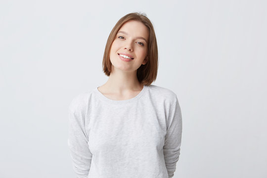 beautiful woman expresses happy emotions, has broad pleasant smile, wears white longsleeve and feels satisfied. Isolated over white background