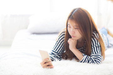 Fototapeta na wymiar Beautiful young asian woman smiling lying relax on the bed in the morning, girl using mobile smart phone talking enjoy, communication and social network concept.