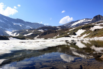 One of lakes on Colle del Nivolet, Graian Alps, Italy, Piedmont, in summertime still with covered with snow and ice with reflection of mountains on calm water surface