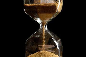 Hourglass with flowing sand on dark background. Time management