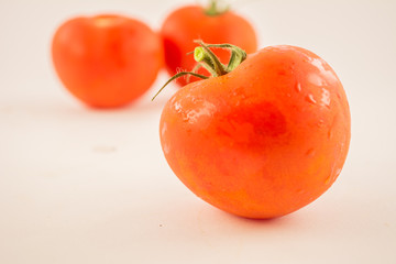 three unpeeled, fresh, red tomatoes with green tails on white background