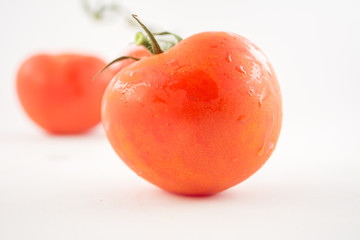 three unpeeled, fresh, red tomatoes with green tails on white background