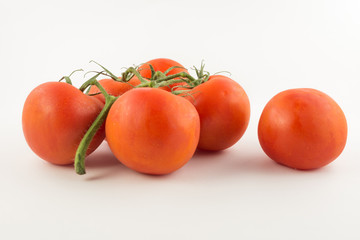 six unpeeled, fresh, red tomatoes with green tails on white background