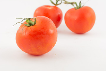 three unpeeled, fresh, red tomatoes with green tails on white background