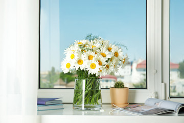 Vase with beautiful chamomile flowers on windowsill