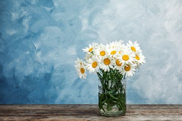 Vase with beautiful chamomile flowers on table against color background