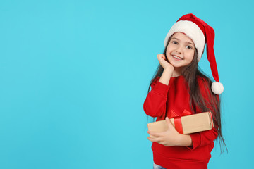 Cute little child in Santa hat with Christmas gift on color background