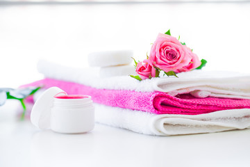 Obraz na płótnie Canvas Spa. Wellness Products and Cosmetics. Towels, cream and pink flowers for a spa relaxation on white background. Natural organic cosmetics for face care. Bath products, bathroom set