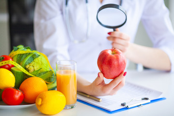 Diet. Doctor Nutritionist hold red apple in her office. Concept of natural food and healthy...