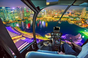 Zelfklevend Fotobehang Helicopter cockpit interior flying on Singapore marina bay with financial district skyscrapers at night reflected on the harbor. Scenic flight above Singapore skyline. Night urban aerial scene. © bennymarty