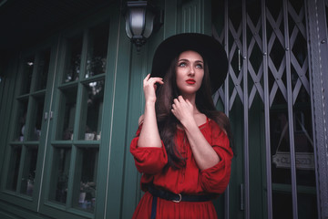 Elegant brunette young woman wearing red dress and straw hat on the street cafe. Fashion and style.
