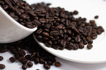 close up coffee beans heap with white cup and saucer . black and brown color seeds background . 